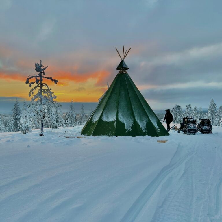 A green kota on a snowy hilltop at sunset