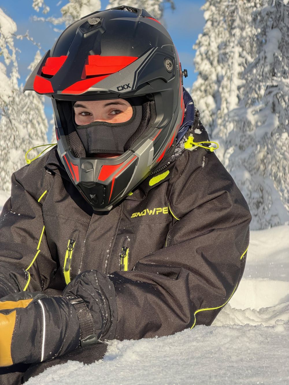Close-up of a guest in a full-face helmet and balaclava, goggles pushed up, in a snowy forest